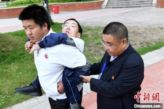 朱金祥背著鐘華強去教室上課的路上，也經常碰到值班的校領導和老師前來搭把手。 卓忠偉 攝