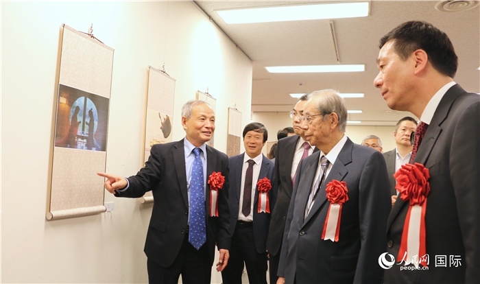 “湖州印象”攝影展主創(chuàng)、世界華人攝影協(xié)會(huì)副會(huì)長馮學(xué)敏向吳江浩大使、福田康夫前首相等嘉賓介紹展出作品。（人民網(wǎng) 許可攝）