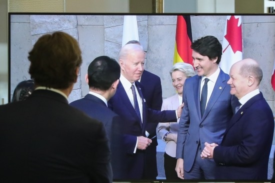 2022年3月24日，在比利時布魯塞爾的北約總部，一名男子觀看屏幕上美國總統(tǒng)拜登（右四）、歐盟委員會主席馮德萊恩（右三）、加拿大總理特魯多（右二）、德國總理朔爾茨（右一）出席七國集團峰會合影儀式的畫面。新華社記者鄭煥松攝