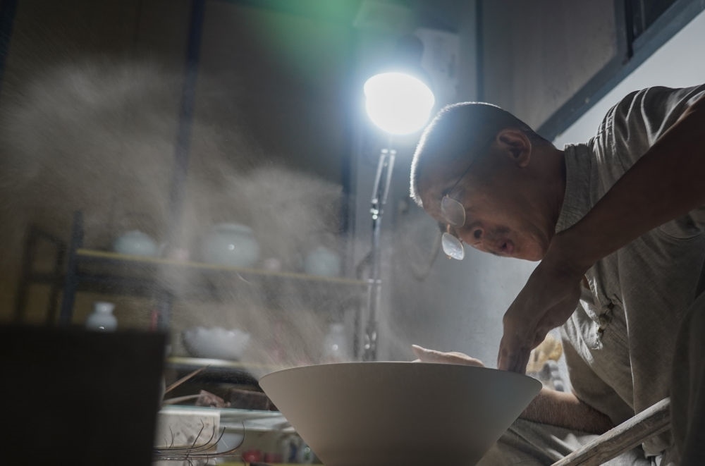 ↑ 在景德鎮(zhèn)，手工匠人吹去坯內(nèi)的泥土（2021年7月14日攝）。