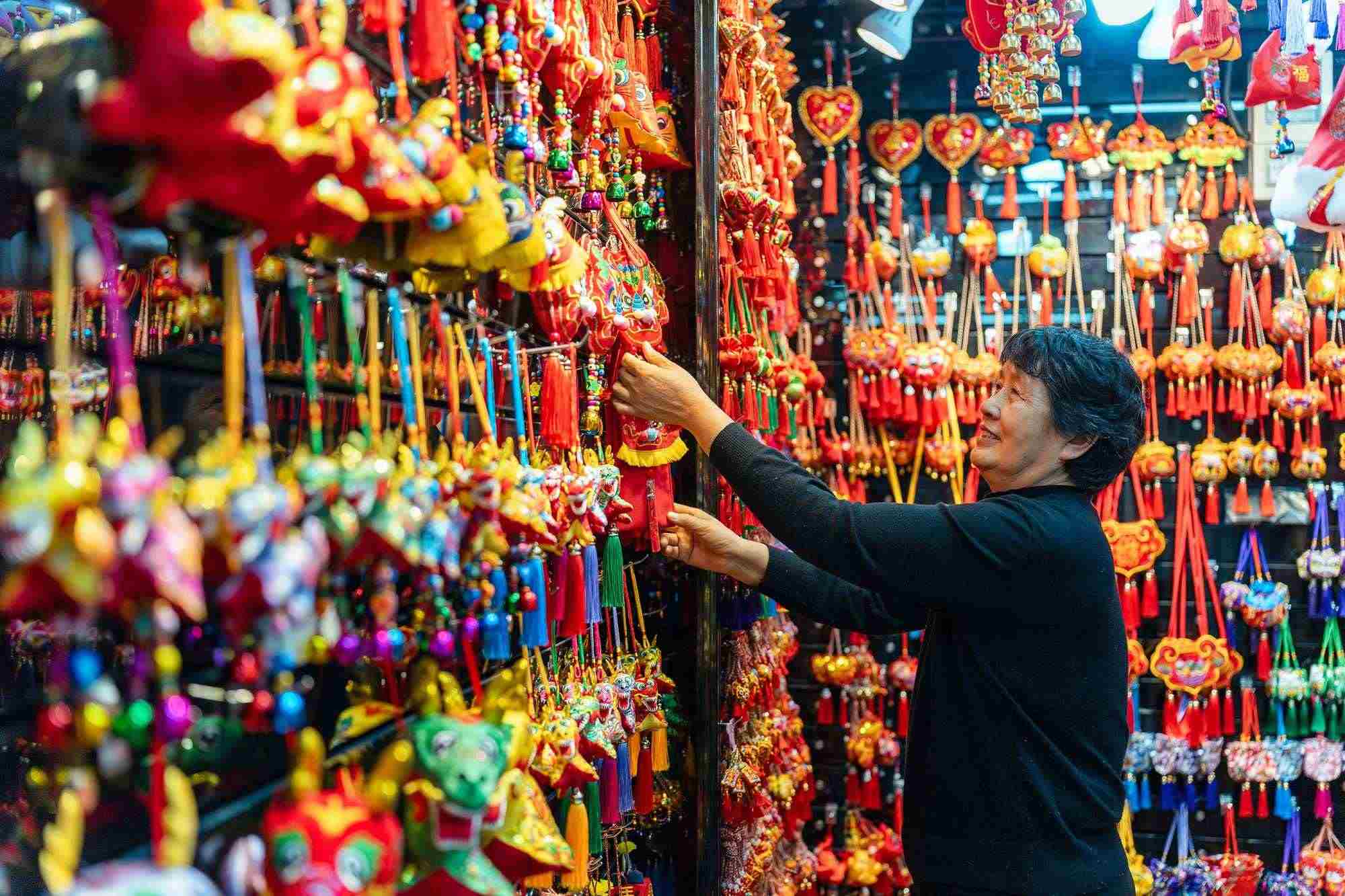 2023年12月11日，金華義烏國際商貿(mào)城，龍年喜慶用品掛滿攤位，顧客正在挑選中。