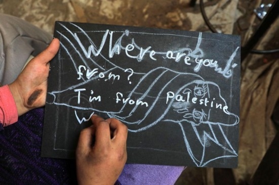 2023年12月28日，一名學生在加沙地帶南部城市拉法一所學校的臨時教室中寫下“我來自巴勒斯坦”的字樣。新華社發(fā)（里澤克·阿卜杜勒賈瓦德攝）