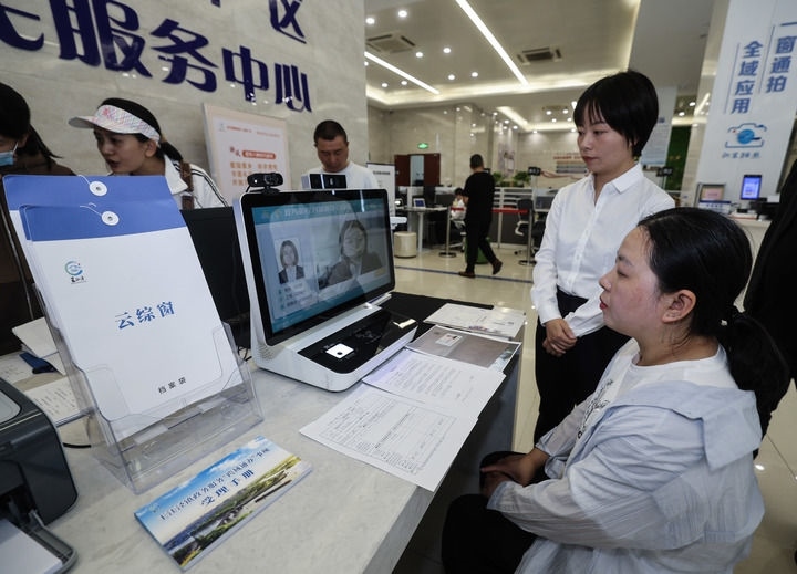 在浙江省嘉興市秀洲區(qū)王江涇鎮(zhèn)便民服務(wù)中心的“跨域通辦·云綜窗”窗口，辦理開(kāi)業(yè)登記的個(gè)體工商戶（右一）通過(guò)該系統(tǒng)與江蘇省蘇州市吳江區(qū)盛澤鎮(zhèn)行政審批局工作人員視頻連線，進(jìn)行身份讀取及材料線上審核（2024年5月9日攝）。新華社記者 徐昱 攝