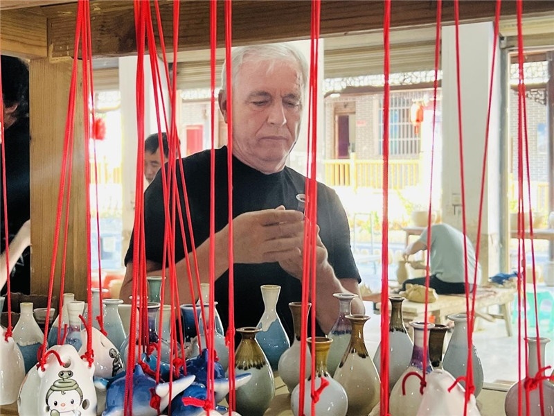 鄉(xiāng)愁如同一根根紅線，將游子與故鄉(xiāng)永遠(yuǎn)地牽連到一起。花茂村陶藝文化創(chuàng)意一條街的母氏陶藝館內(nèi)，紅線吊著陶瓶，思緒游走萬(wàn)里。摩爾多瓦“信息標(biāo)簽”通訊社社長(zhǎng)亞歷山大·塔納斯端詳著館內(nèi)展示的陶藝作品，并挑選出心儀的小擺件帶回摩爾多瓦，也帶走花茂村的“鄉(xiāng)愁”。（張亞欣攝）