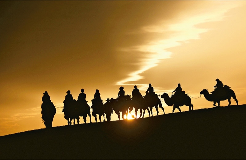 新時代以來，文化和旅游深度融合發(fā)展體制機制不斷健全，成功走出了一條獨具特色的中國旅游發(fā)展之路。圖為2024年9月1日清晨，游客在甘肅省敦煌市鳴沙山月牙泉景區(qū)乘騎駱駝，欣賞大漠風光，體驗絲路風情。 新華社發(fā) 張曉亮/攝