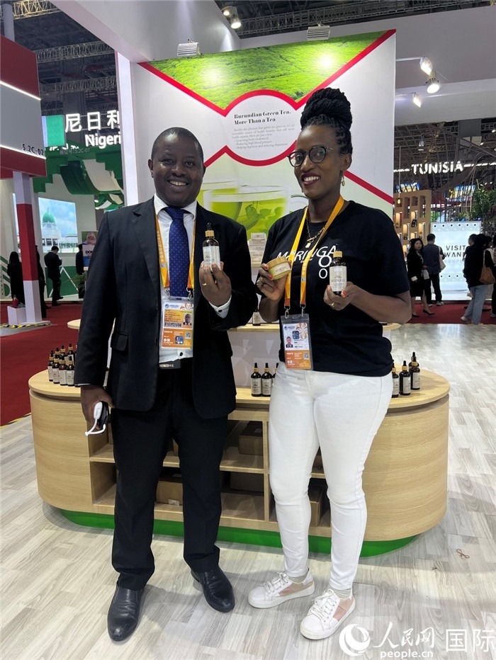 6月6日，布隆迪駐華大使館一等參贊布利馬索·阿爾弗雷德 (左，Bulimaso Alfred) 和參展商卡馬里扎·埃斯特拉 (Kamariza Estella) 在第七屆中國國際進口博覽會布隆迪館展示當?shù)厣a(chǎn)的辣木油。（人民網(wǎng) 艾里士 攝）